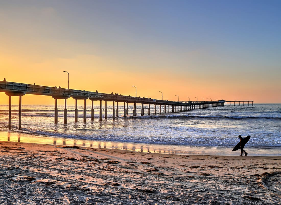 San Diego, CA - Aerial View of a Man Walking on a Beach With a Surf Board During Sunrise